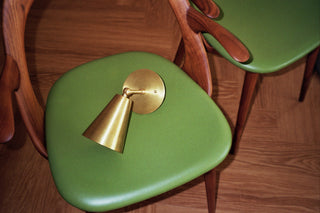 Green chair with a brass bell-shaped light on a wooden floor